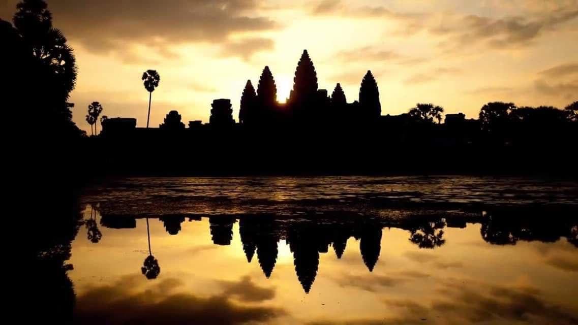 Angkor Wat's towers in golden silhouette, reflected in the temple pool at sunrise